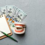 flat lay composition with educational dental typodont model money with notebook colored table top view expensive treatment