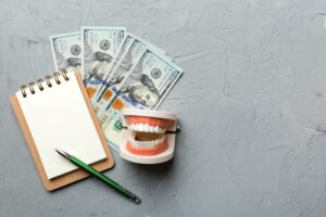 flat lay composition with educational dental typodont model money with notebook colored table top view expensive treatment